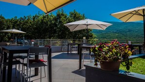 Eine Terrasse im Freien mit Tischen, Stühlen, Sonnenschirmen und einem Blumentopf.