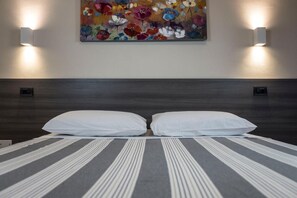 A hotel room with a large bed, two wall-mounted lights, and a colorful floral painting above the bed. - Foresteria La Merlina (Dernice)