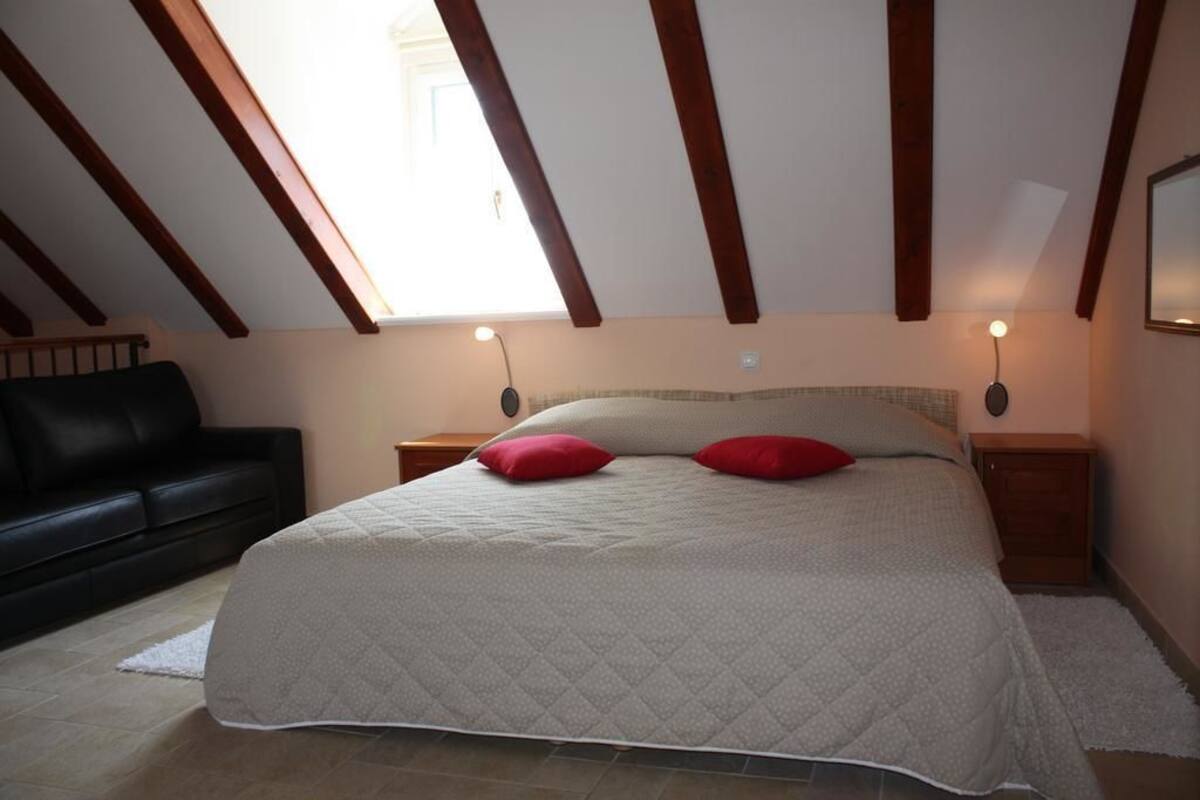 Ein Schlafzimmer mit einem Bett, zwei Nachttischen, einem schwarzen Sofa und einem Oberlicht.