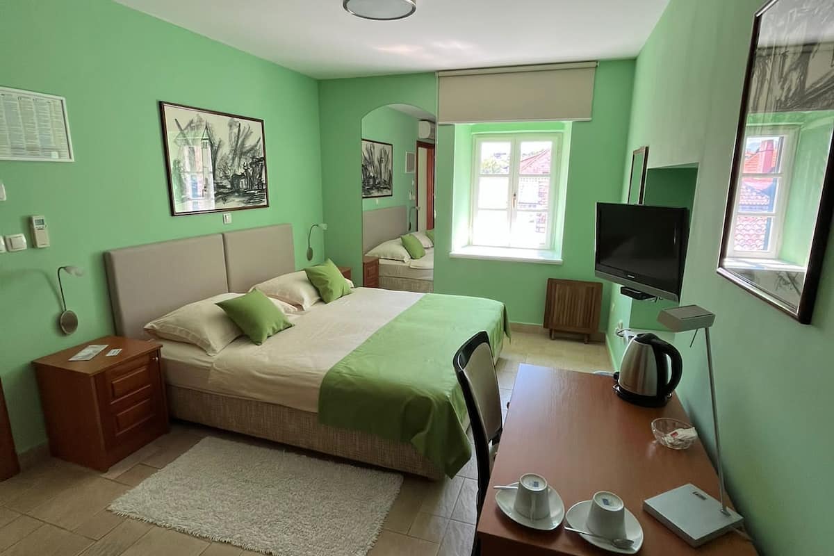 Ein Schlafzimmer mit Bett, Nachttisch, Sessel, Schreibtisch und Fernseher.
