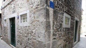 Un bâtiment en pierre avec une porte et des fenêtres vertes, et une enseigne bleue sur le mur.