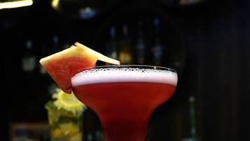 Un cocktail servi dans un verre à martini, agrémenté d’un fruit, sur le comptoir en bois d’un bar.