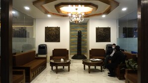 A lobby with a chandelier, two sofas, two round tables, and a tall pillar. - Hotel Tapas (Kathmandu)
