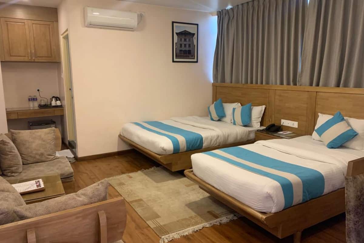 Quarto de hotel com duas camas, um sofá, uma mesinha, um aparelho de ar condicionado e um quadro na parede.