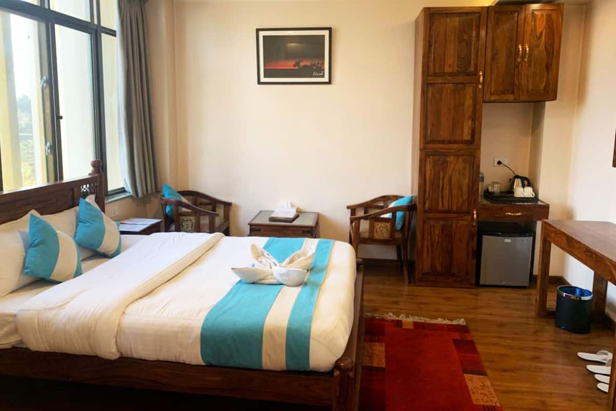 Quarto de hotel com uma cama, duas cadeiras, uma mesa pequena, uma escrivaninha, um frigorífico e um quadro na parede.