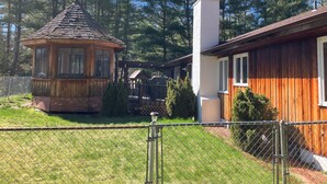 Une cabane en bois avec un toit de chaume, une cheminée et une cour clôturée agrémentée d’un petit kiosque.