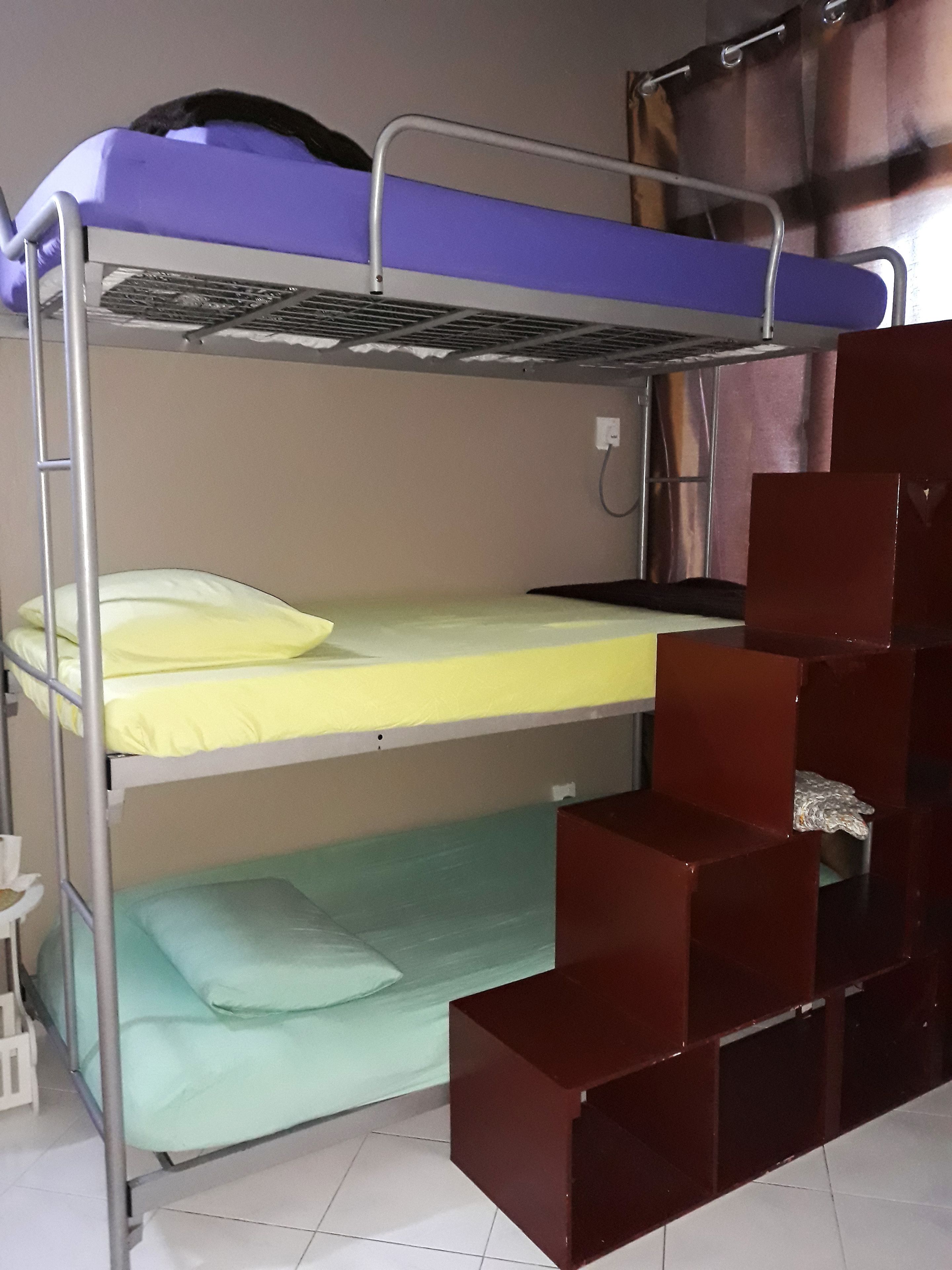 A bunk bed with a metal frame, a lower bunk with a green mattress, and a top bunk with a blue mattress.
