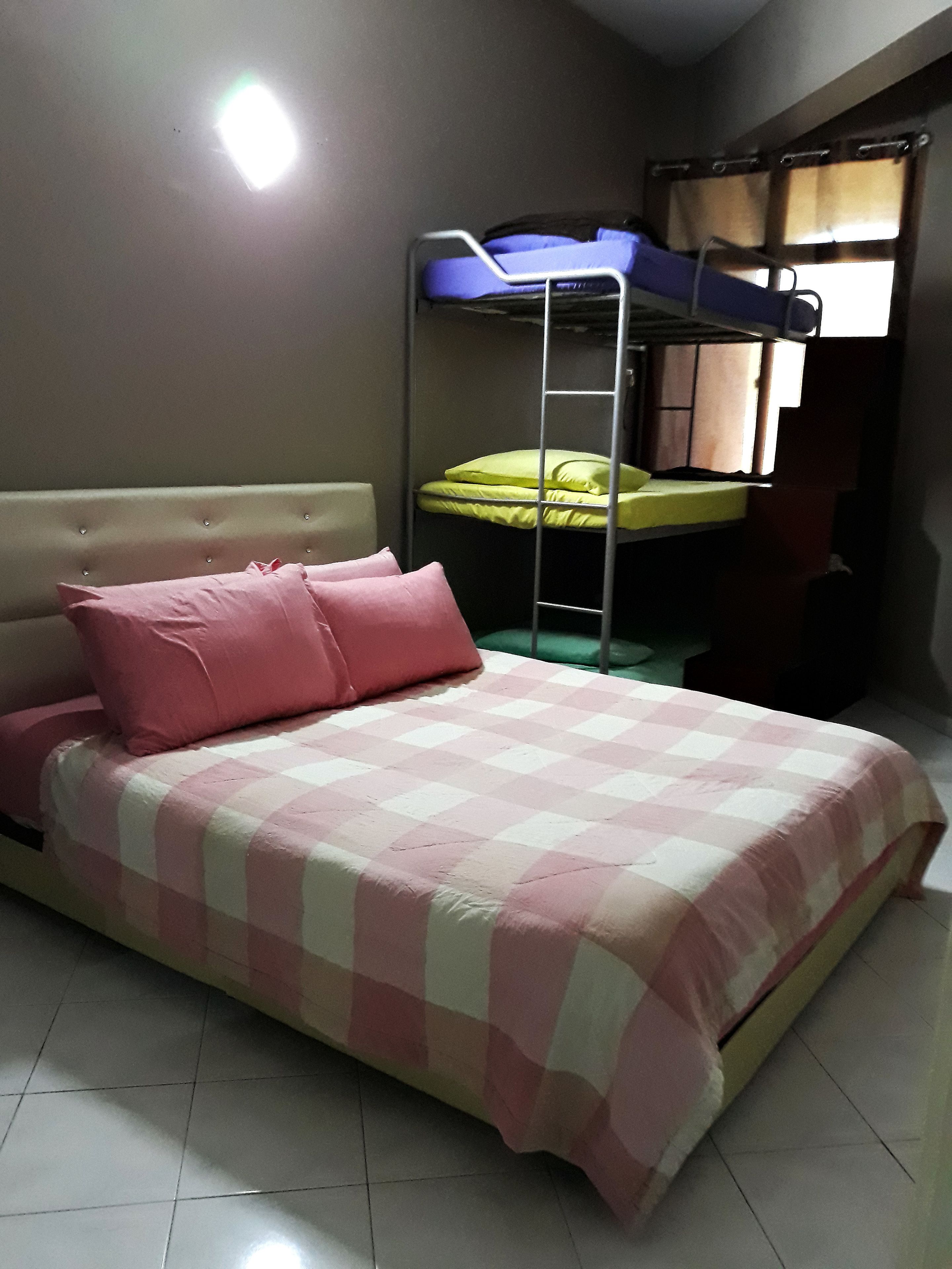 A single bed with a pink and white checkered bedspread, a headboard, and two pink pillows.