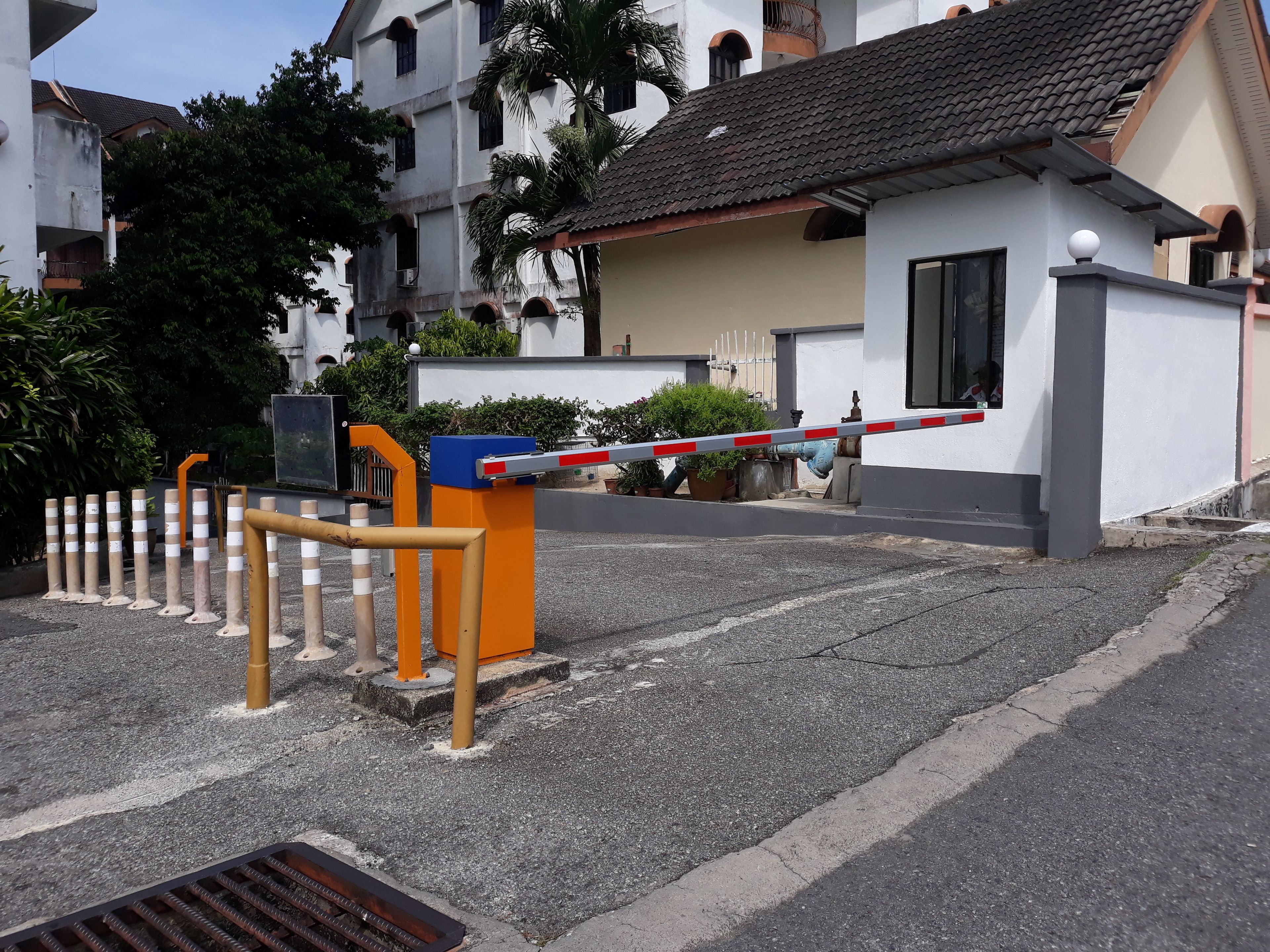 Une entrée sécurisée, dotée d’une barrière, de bornes et d’une boîte de sécurité bleue.