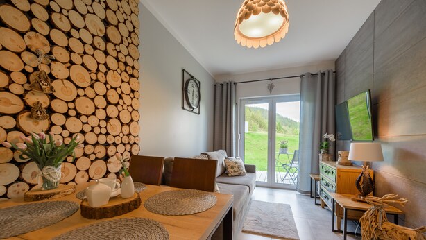 Una sala de estar moderna con una pared de troncos de madera, una zona de comedor con mesa de madera y un sofá.