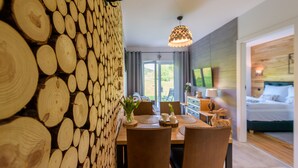 Un comedor moderno con pared de madera rústica, una mesa de comedor con sillas y vista a un dormitorio con cama y televisor.