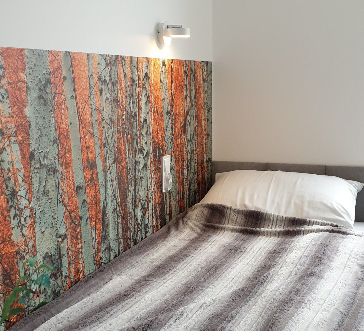 A bedroom with a bed, a wall with a textured pattern, and a wall-mounted light fixture.