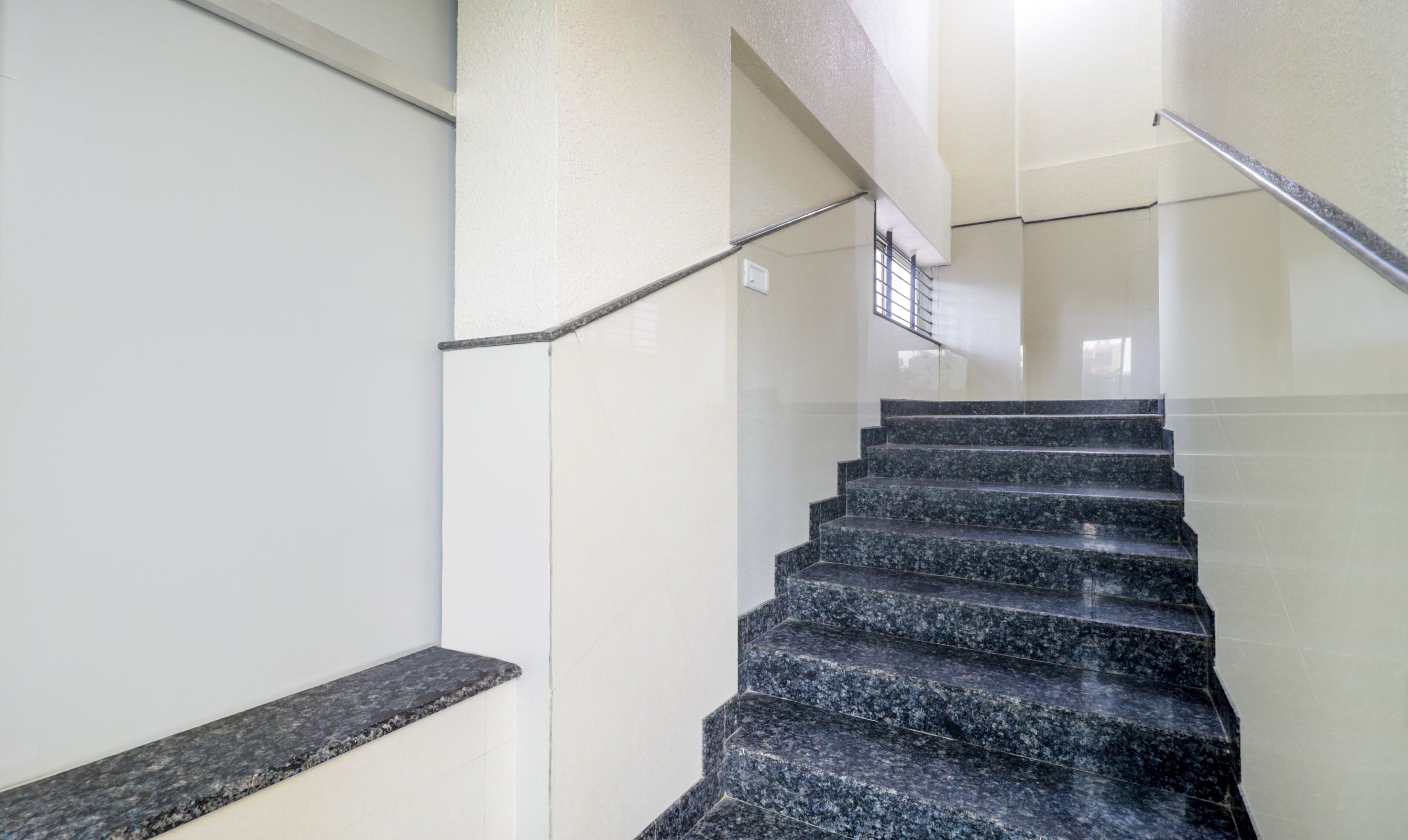 A staircase with black granite steps and a metal handrail, leading to a landing with a glass door.