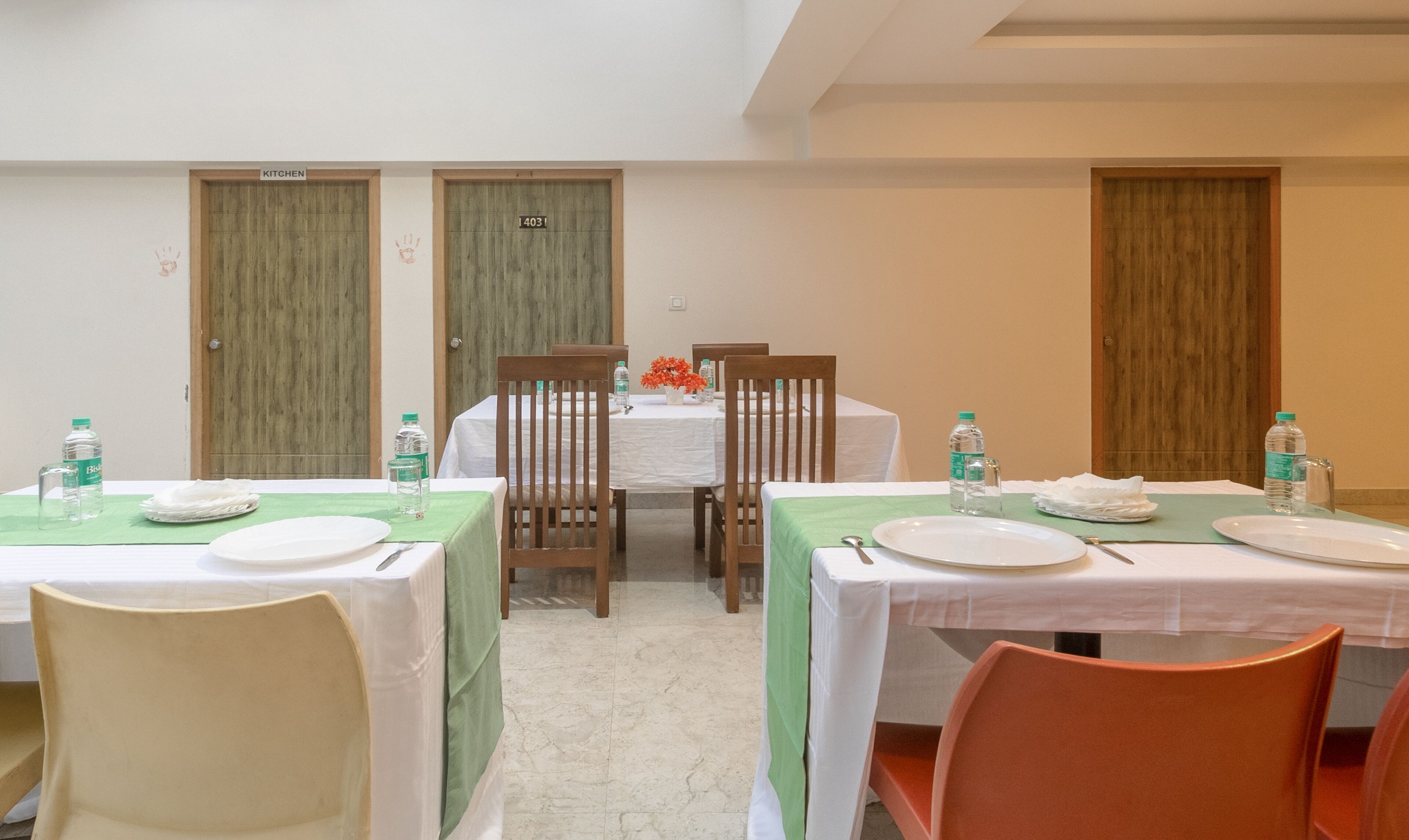 A dining area with tables set for four, each with a white tablecloth, chairs, plates, and water bottles. There are two wooden doors labeled "KITCHEN" and a number "4031".