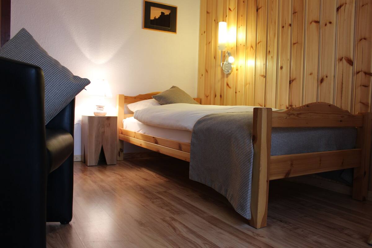 Un lit en bois avec une tête de lit, une table de chevet avec une lampe et une chaise avec un coussin.