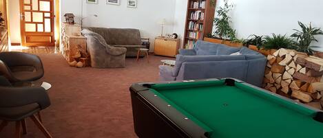 Una sala de estar acogedora con una mesa de billar, un sofá, una silla y una estantería.