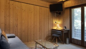 Ein modernes Wohnzimmer mit einer Couch, einem Glastisch, einem Schreibtisch mit Lampe und einem an der Wand montierten Fernseher.
