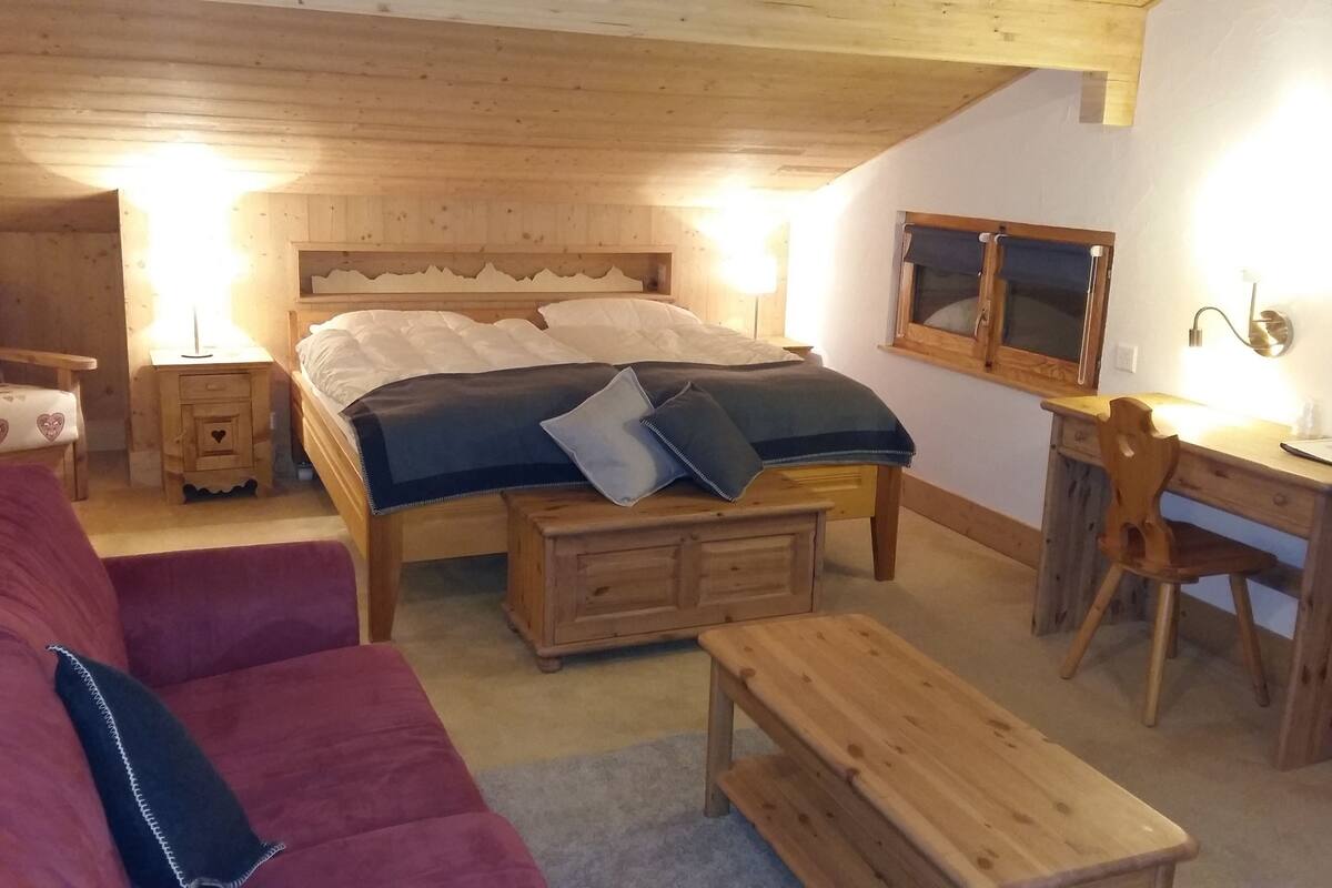 Une pièce chaleureuse avec un lit en bois, un bureau en bois, un canapé rouge et un banc en bois.