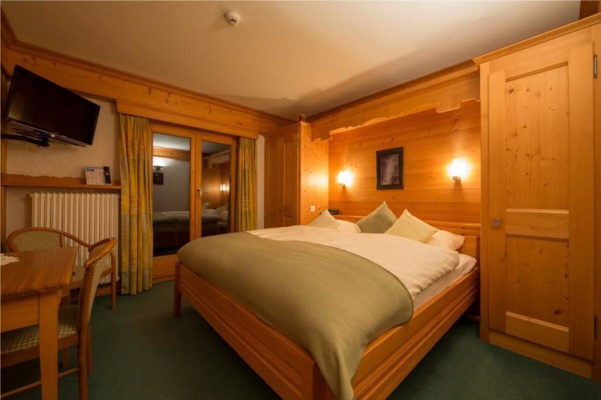 Une pièce en bois avec un lit, un bureau et une chaise, un téléviseur et une porte.