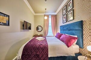 Una habitación de hotel con una cama grande, una mesita de noche, un espejo y una pared con cuadros.