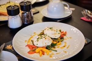 Un plato de comida con huevos pochados, verduras y salsa, acompañado de saleros y pimenteros sobre una mesa.