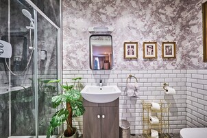 Un baño con cabina de ducha de vidrio, un lavabo con salpicadero de mármol y un espejo con marco dorado.