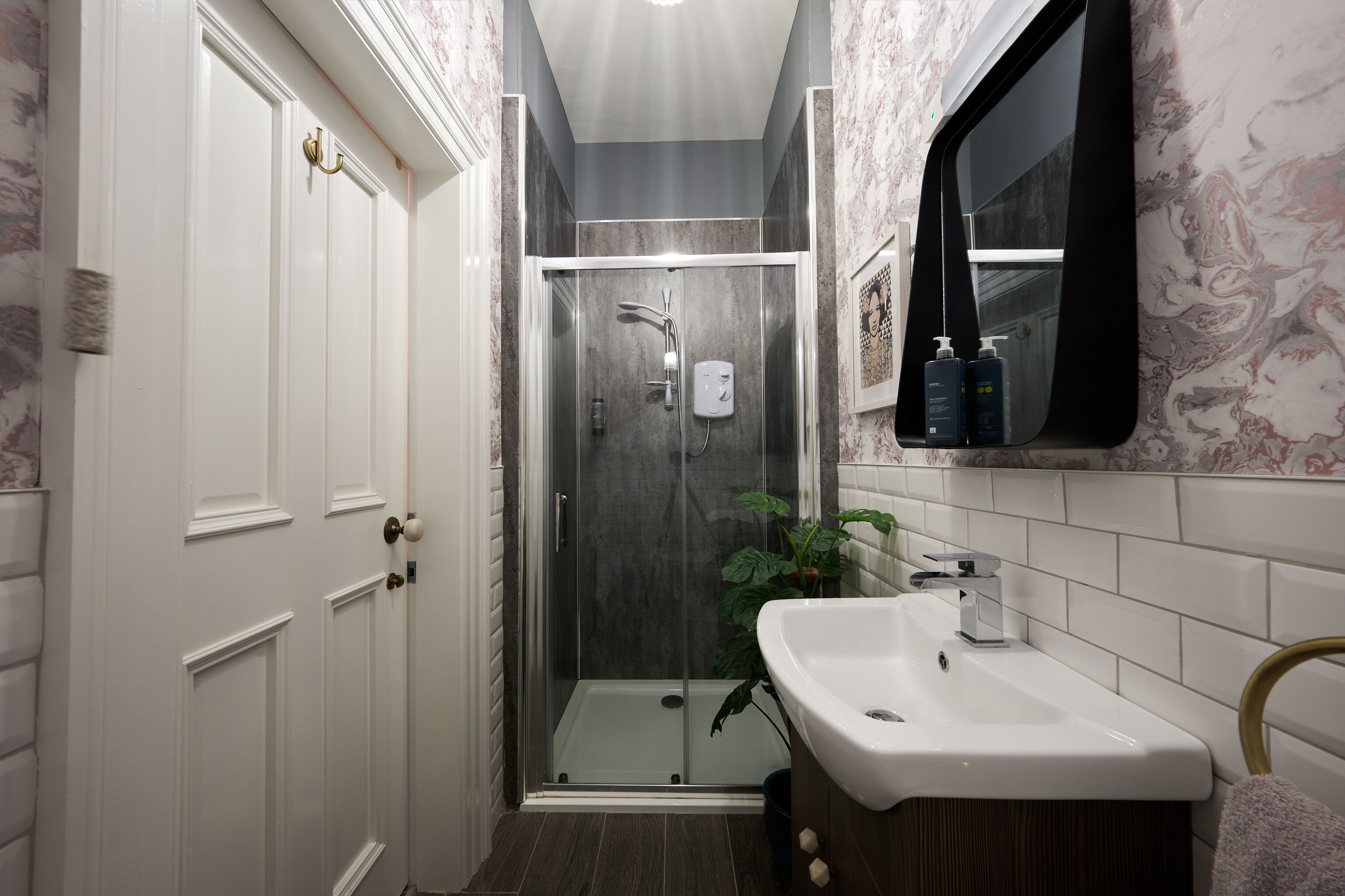 A narrow bathroom with a glass-enclosed shower, a white sink, and a mirror above it.