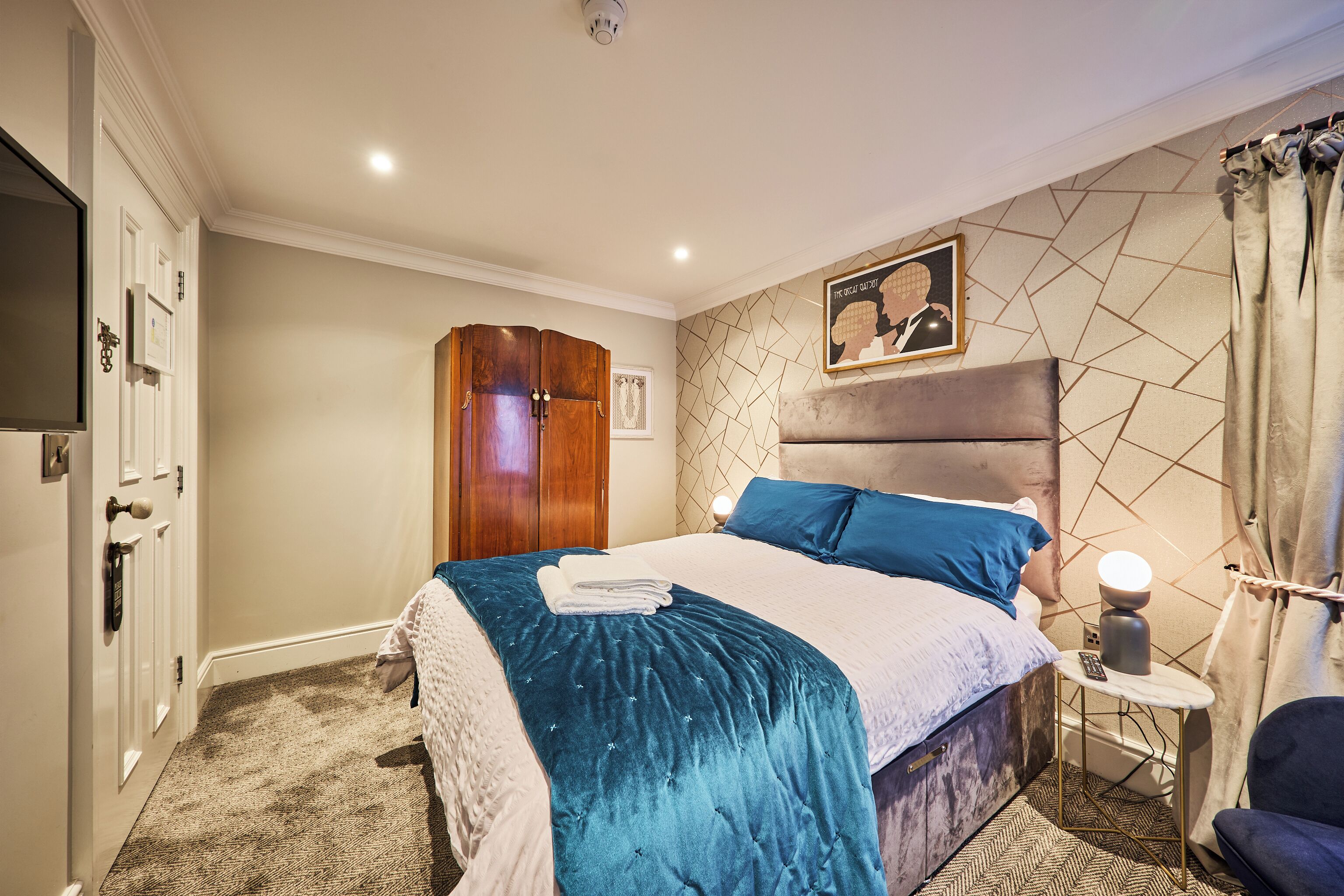 A hotel room with a bed, a wardrobe, a bedside table with a lamp, and a picture on the wall.