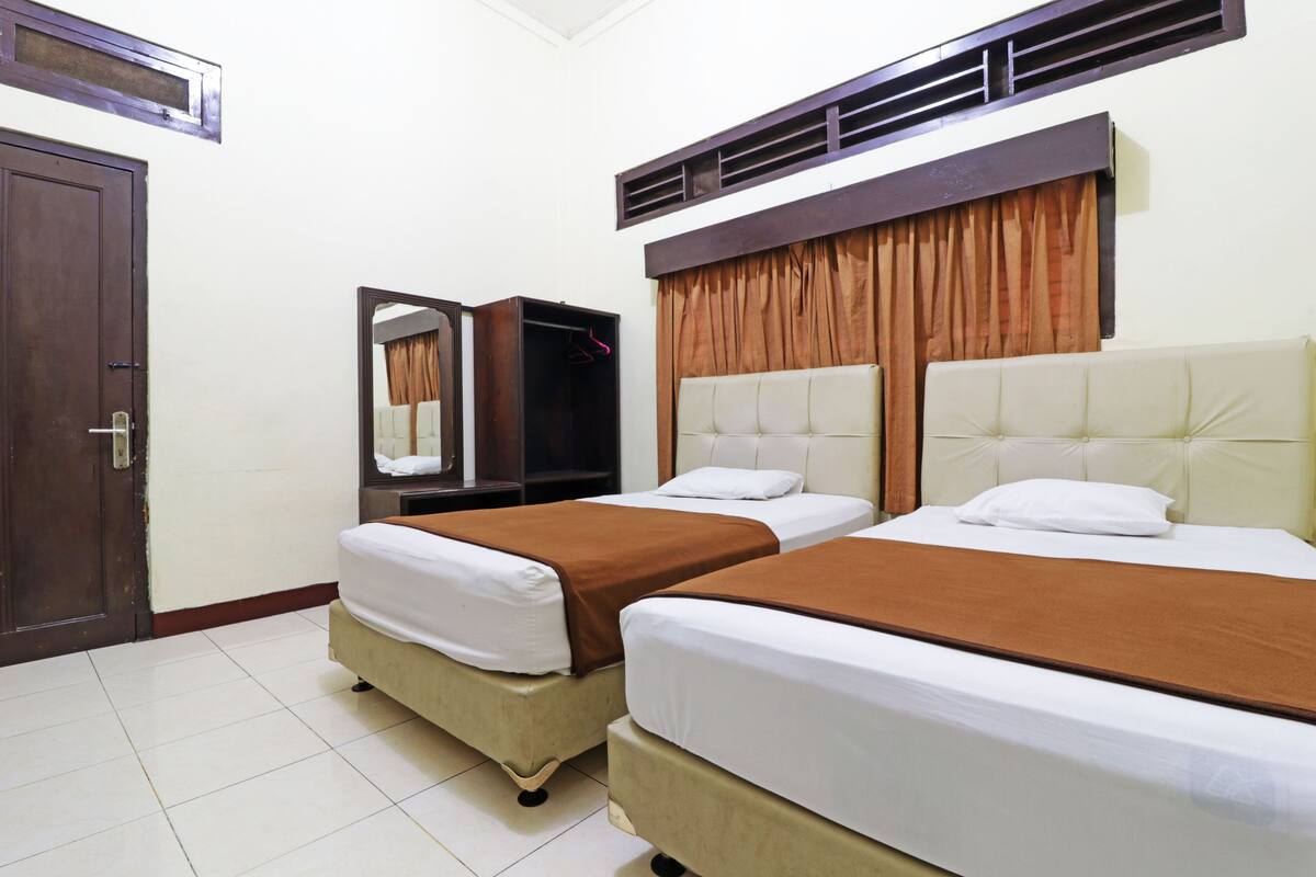 A hotel room with two beds, a wardrobe, a mirror, and a door.