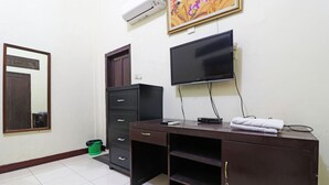 Una habitación con un escritorio de madera oscura, un televisor de pantalla plana montado en la pared, un espejo, un armario y un cubo de basura verde.