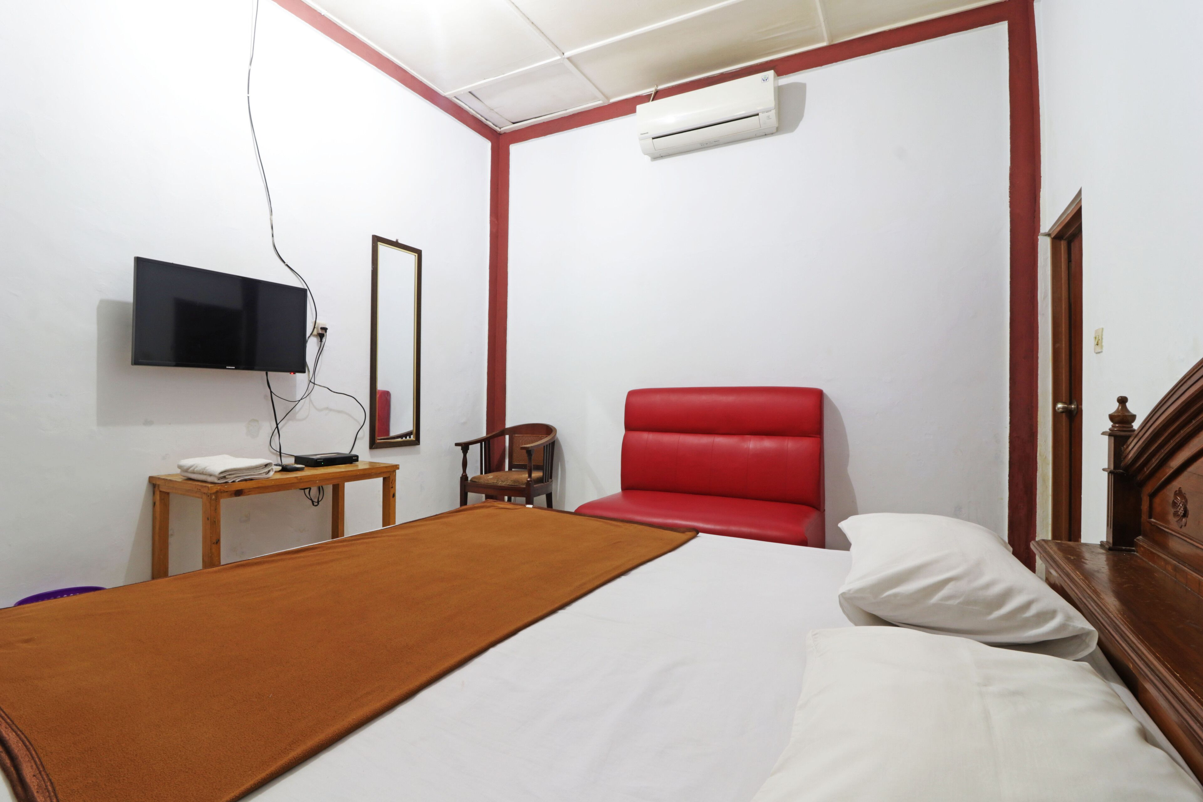 A bedroom with a bed, a red chair, a television, and a mirror.