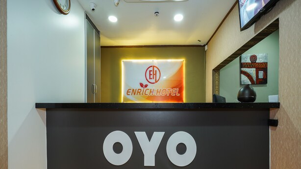 A reception desk with a sign for Enrich Hotel and a large OYO logo. - Enrich Hotel (Sungai Buloh)