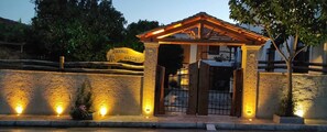 Estructura de piedra con techo de madera y una puerta, con el letrero "Orange Garden", y luces a lo largo de la base.