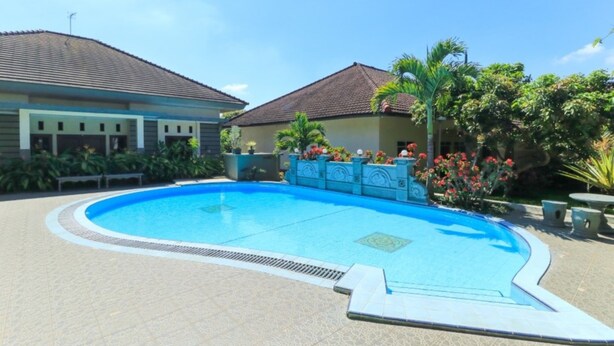 A swimming pool with a tiled deck, surrounded by a low wall and potted plants. - Villa Bunga (Batu)