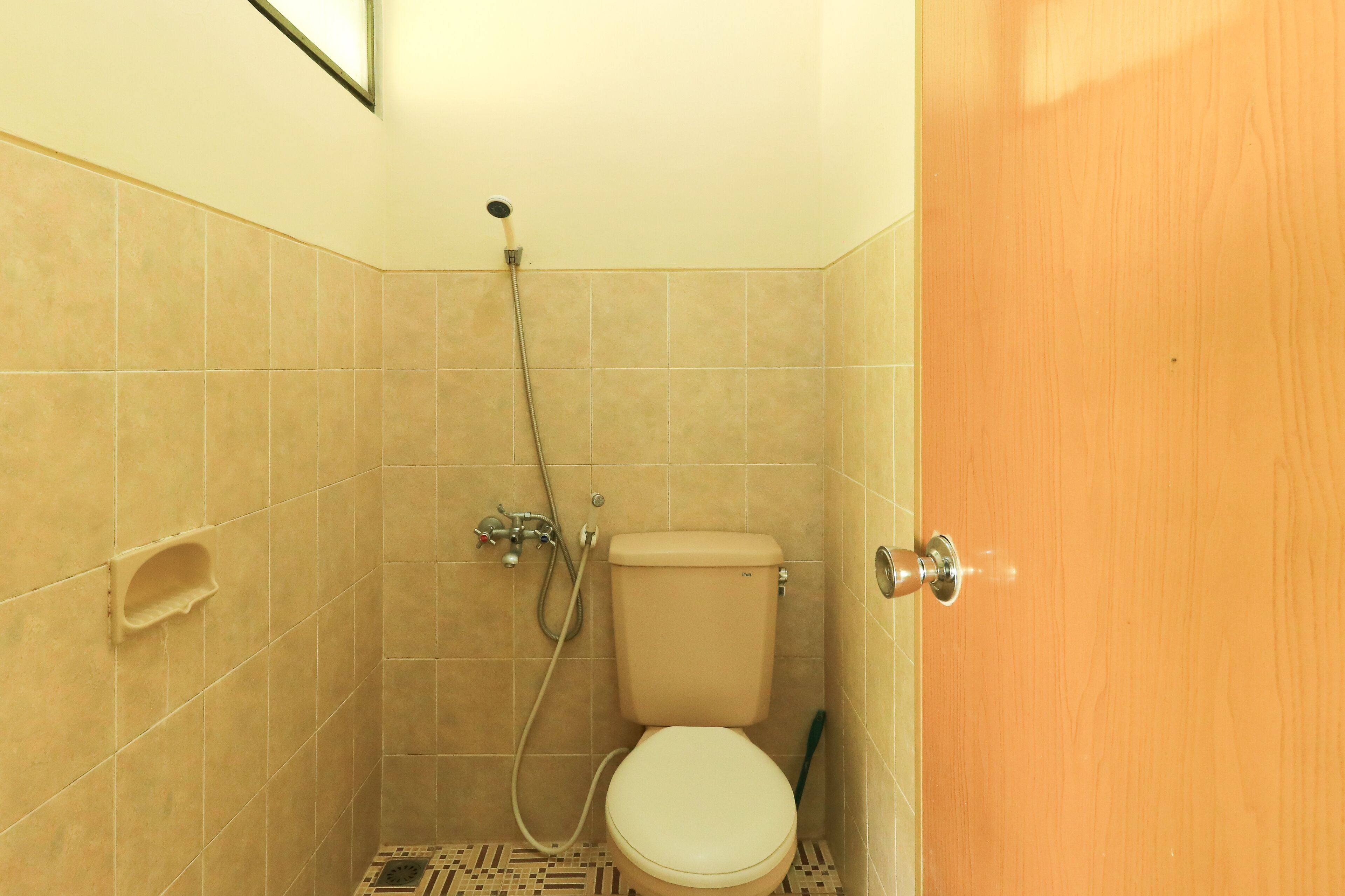 A small, tiled bathroom with a toilet, shower, and a wooden door.