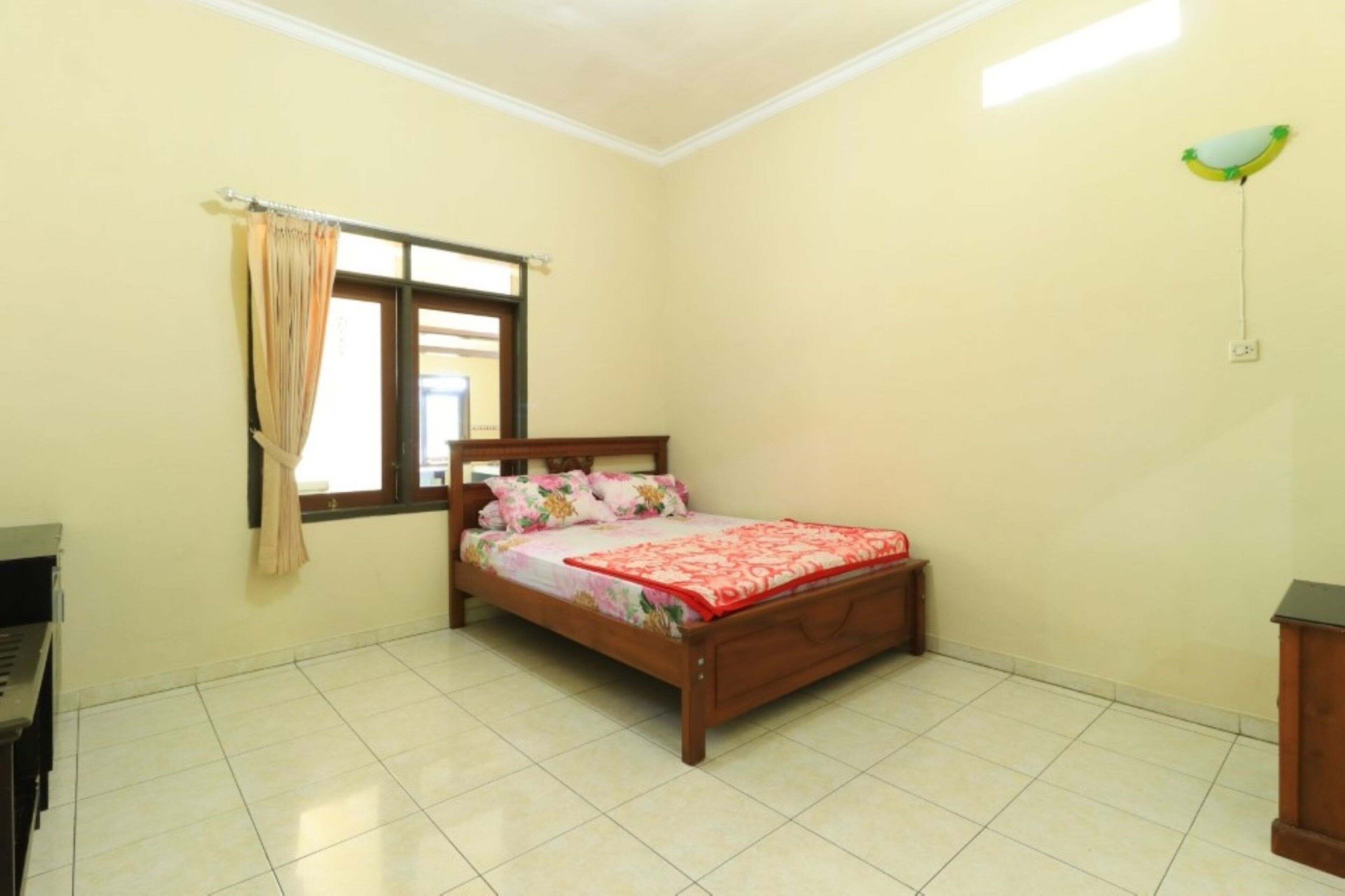 A bedroom with a bed, curtains, a window, and a wall-mounted light fixture.