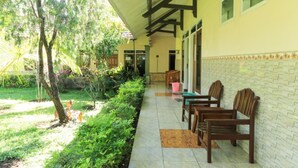 A covered outdoor seating area with chairs and tables, a tiled floor, and a garden with trees and plants. - Villa Bunga (Batu)