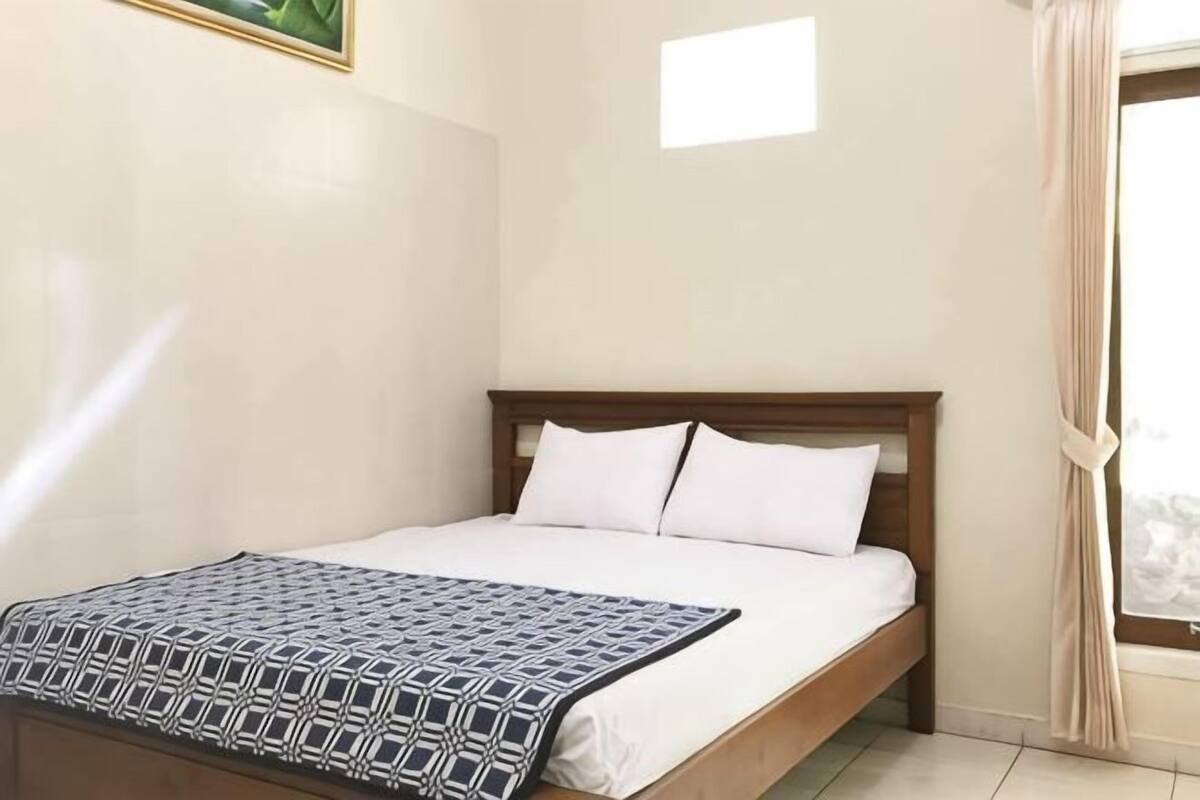 Una cama individual con cabecera de madera, una colcha con estampado y una ventana con cortinas.