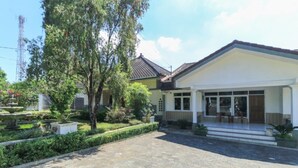 A two-story house with a tiled roof, a front porch, and a garden with a fountain. - Villa Bunga (Batu)