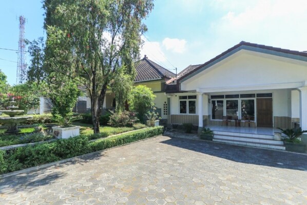 Ein zweistöckiges Haus mit Ziegeldach, einer Veranda und einem Garten mit Brunnen.