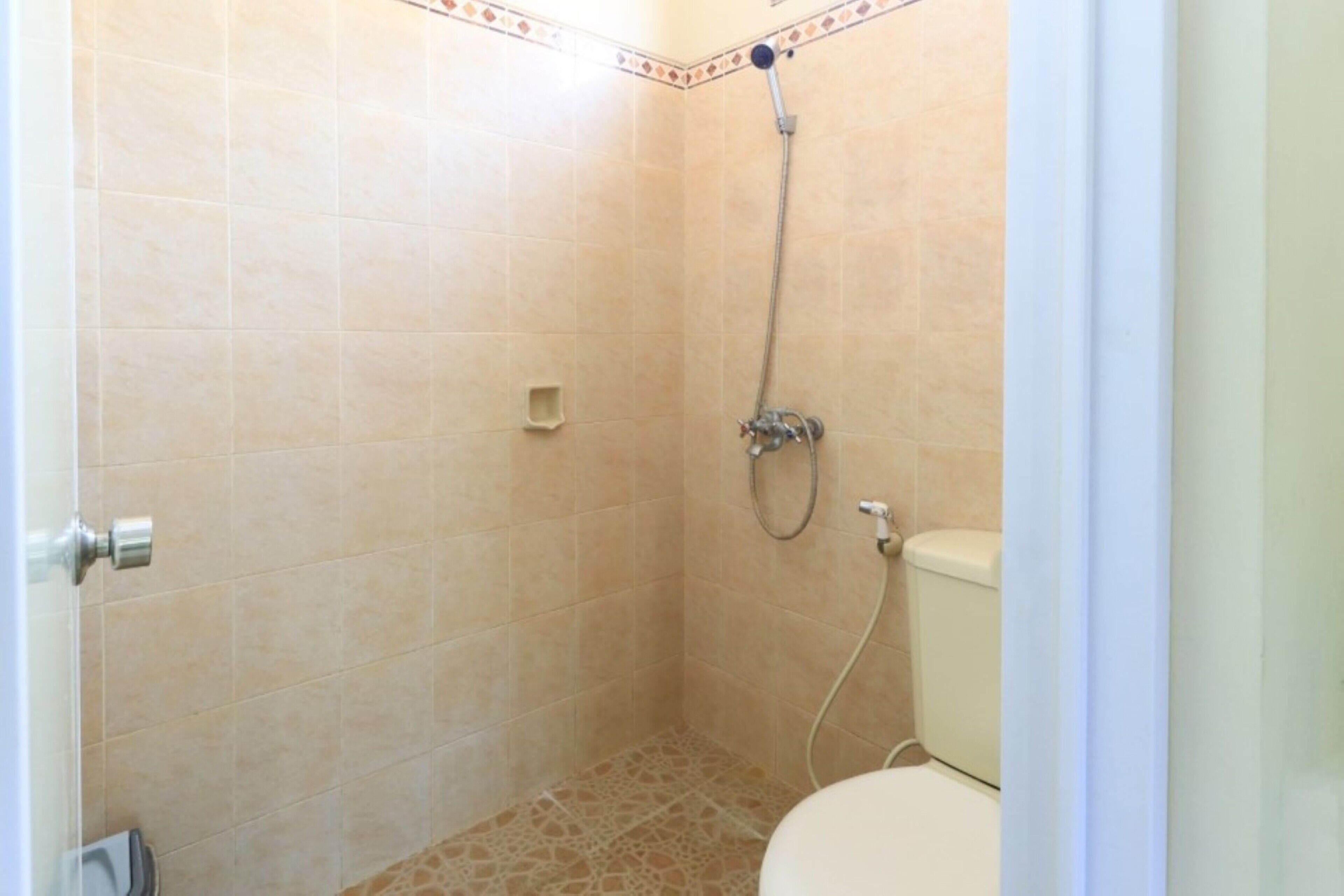 Ein kleines Badezimmer mit Fliesen, einer Dusche, einer Toilette und einer Tür.
