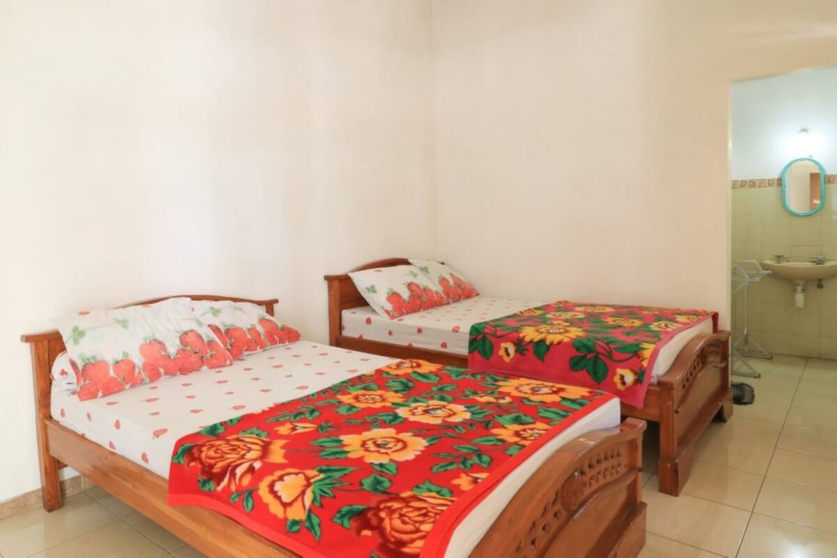 Two wooden beds with floral bedspreads, a small bathroom with a sink and mirror, and a tiled floor.