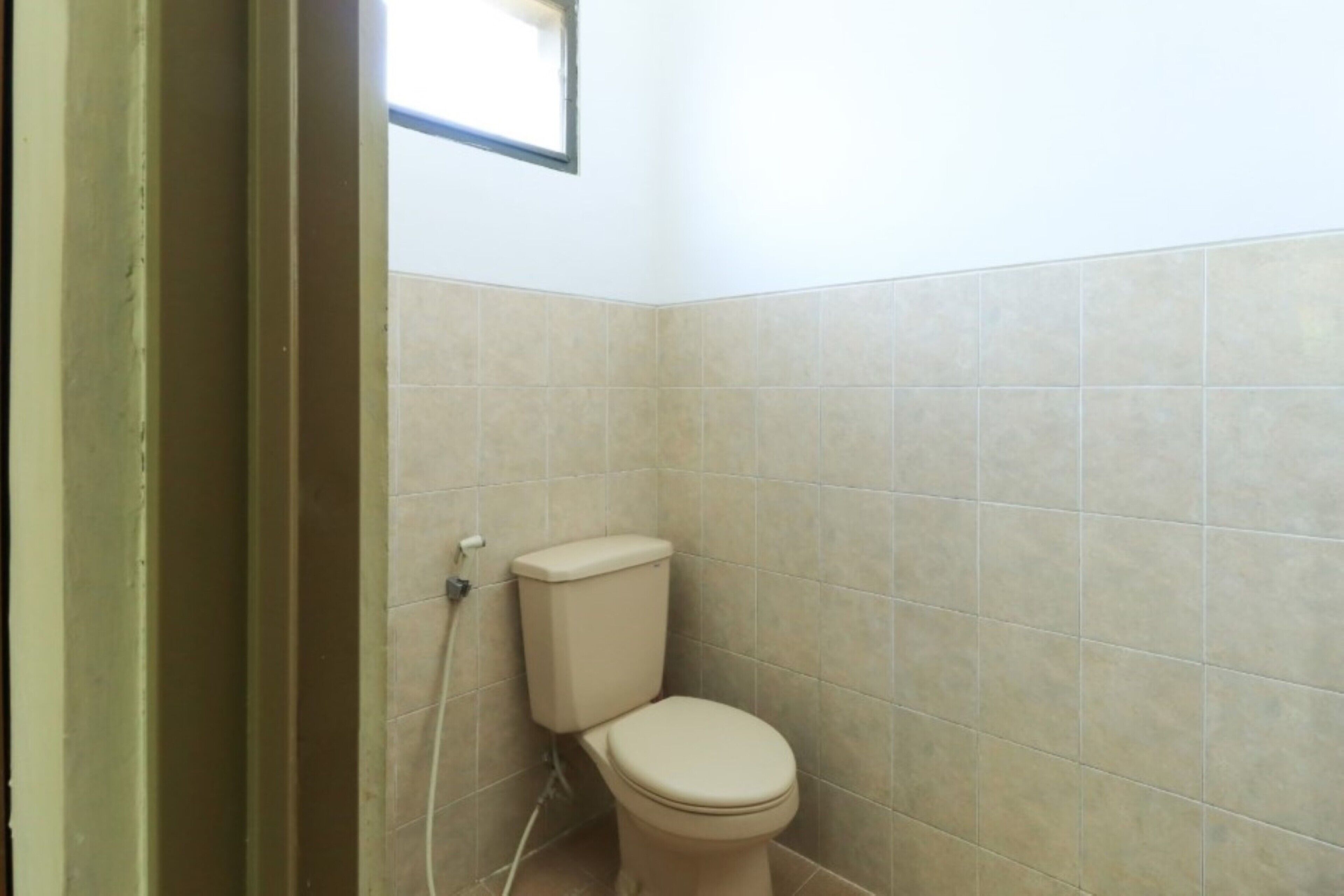 Een kleine, schone badkamer met toilet, betegelde wanden en een raam boven het toilet.