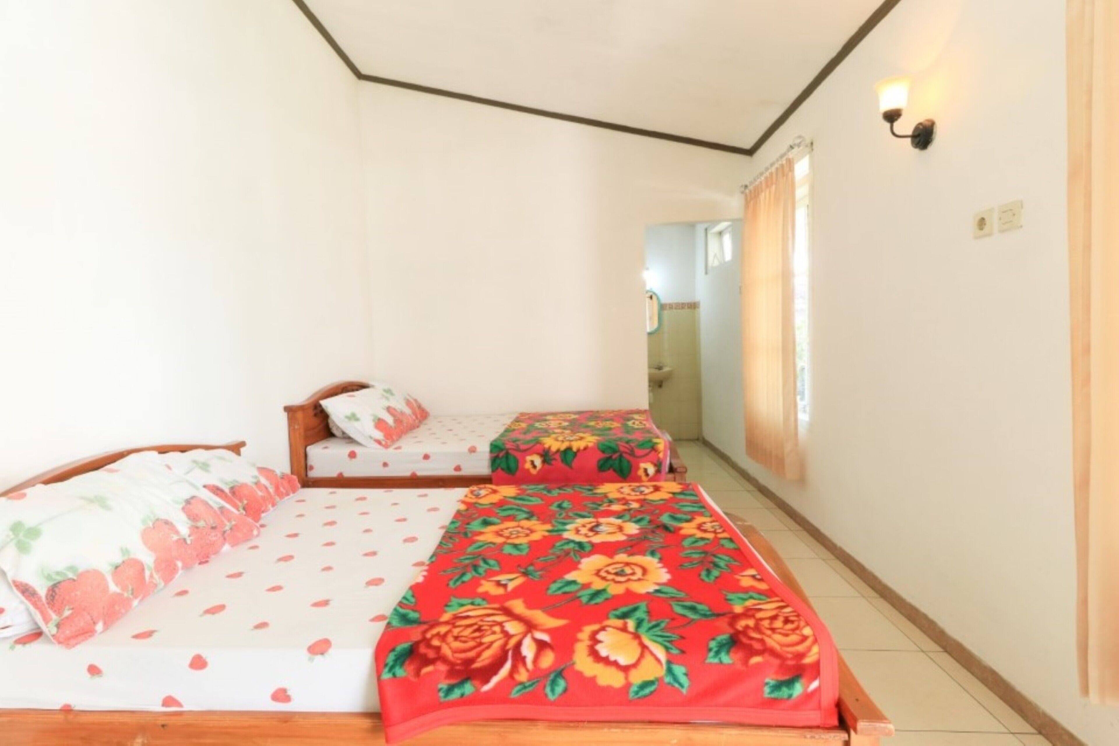 Une chambre avec deux lits, l’un recouvert d’une couvre-lit à motifs floraux et l’autre d’une couvre-lit à motifs de fraises.
