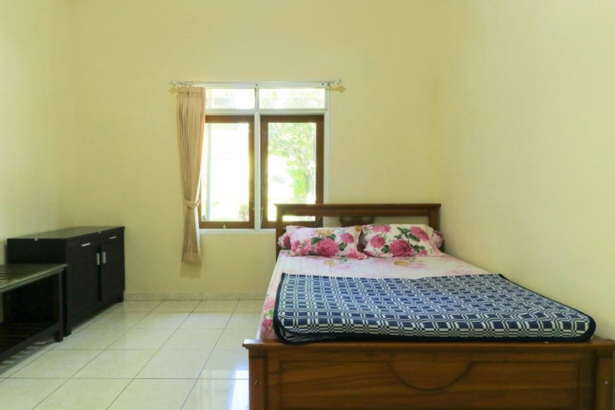 A bedroom with a bed, a nightstand, a dresser, and a window with curtains.