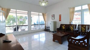 A spacious living room with a wooden coffee table, a sofa, and a dining table. There are large windows with curtains, a refrigerator, and a chandelier. - Villa Bunga (Batu)