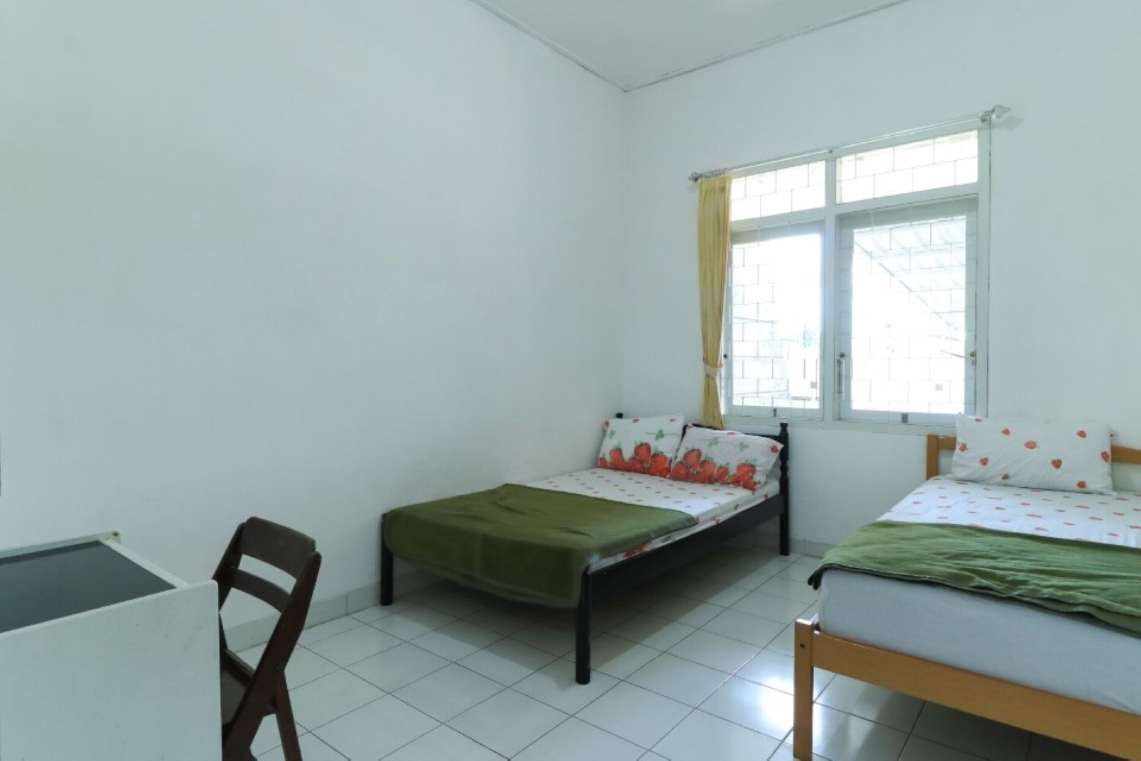 Una habitación pequeña y limpia con dos camas individuales, un escritorio y una silla.