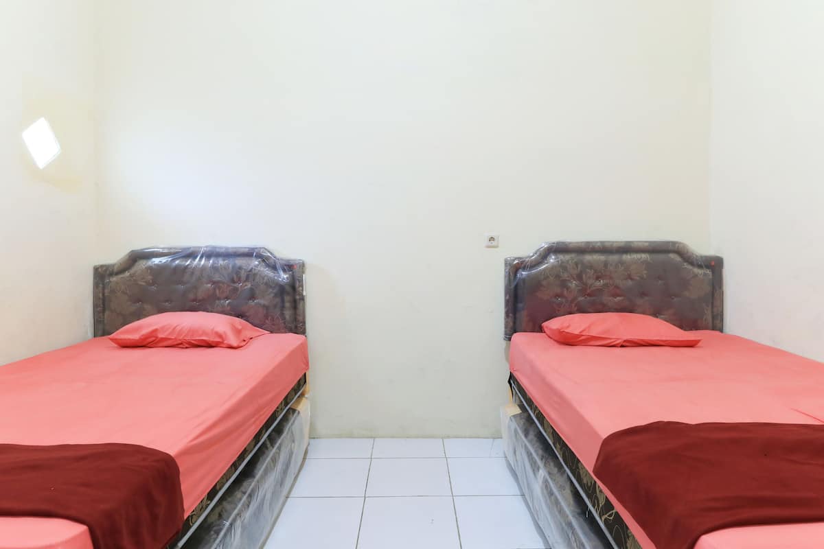 Two single beds with red bedding in a small room with white walls and a tiled floor.