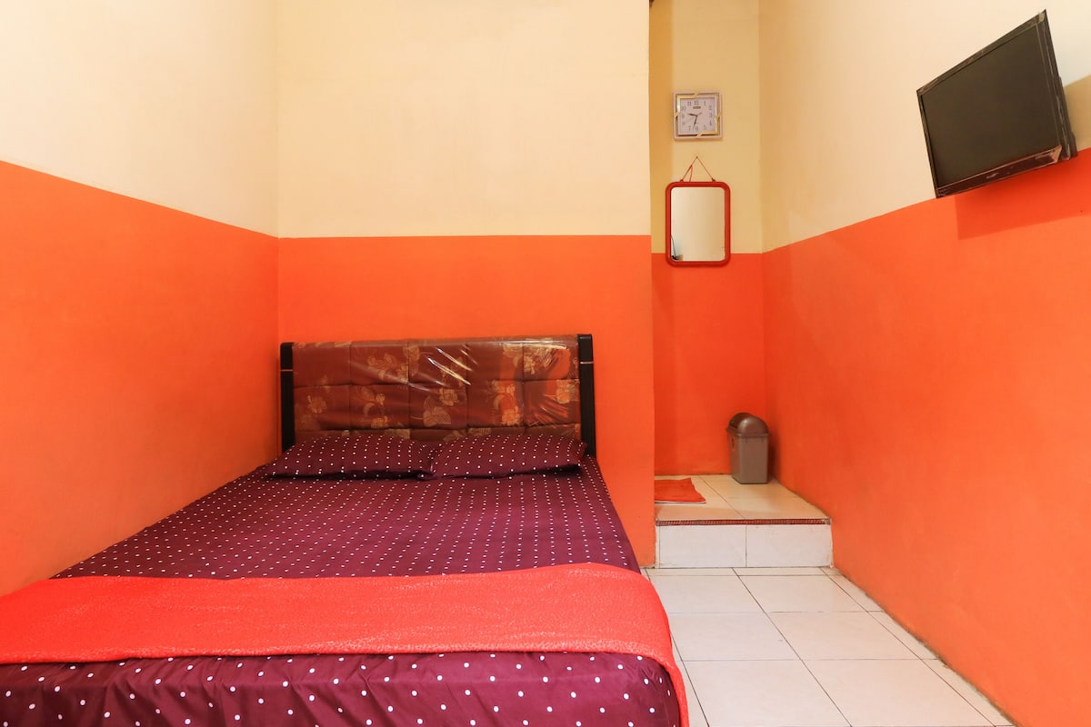 A small, brightly colored room with a bed, a wall clock, and a television.