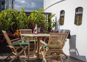 An outdoor seating area with wooden chairs and a table, surrounded by potted plants and flowers. - Fingal - A Luxury Floating Hotel (Edinburgh)